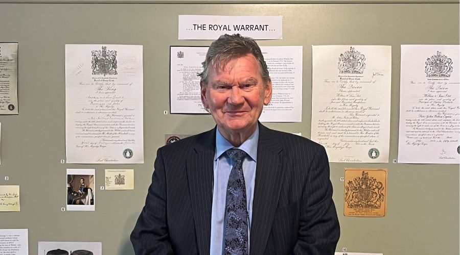 Walter Scott, of Wilkin and Sons, standing in front of a wall of Royal Warrants